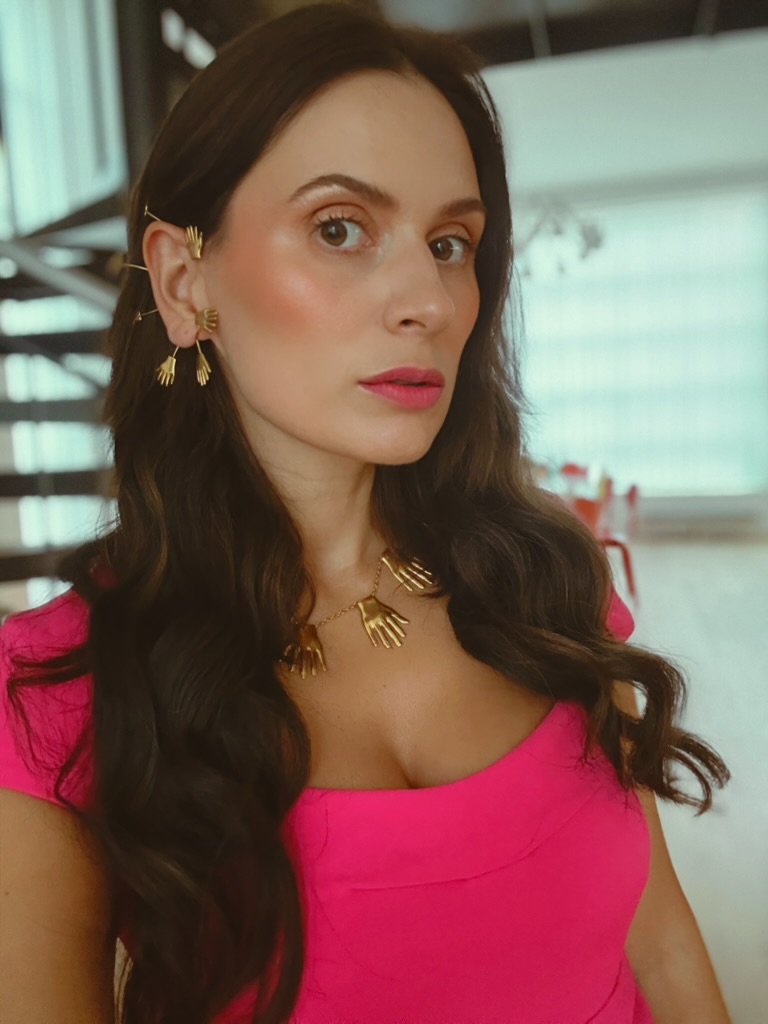 Portrait of Sahra-Josephine Hjorth wearing a pink dress with gold hand-motif jewelry