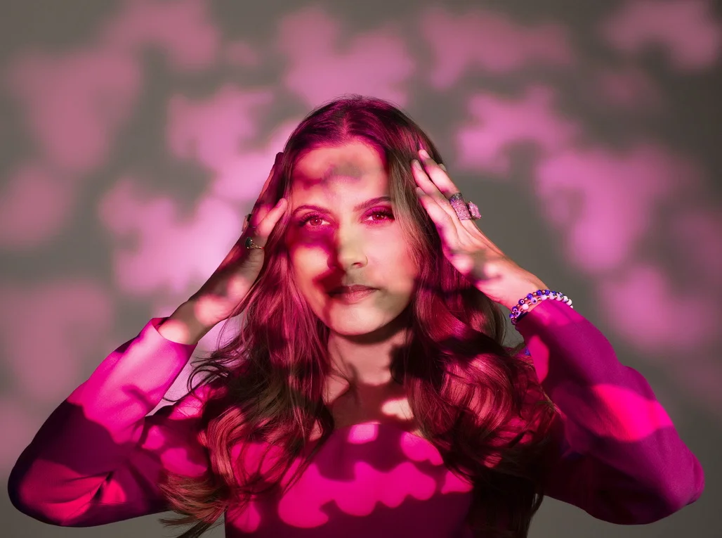 Sahra-Josephine with hands at her head in pink patterned light