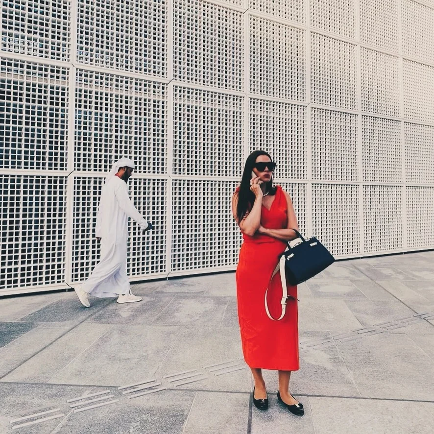 Sahra-Josephine in a red dress on the phone by a white lattice wall